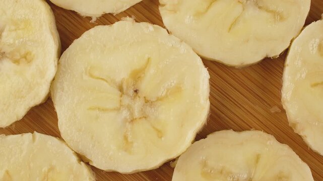 Top view of fresh banana slices pattern rotating on a wooden board. Healthy organic fruit background.