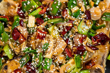 A close-up of spicy stir-fried dish with chili, garlic, sesame seeds, green onions, and tofu or meat, showcasing bold Asian flavors.