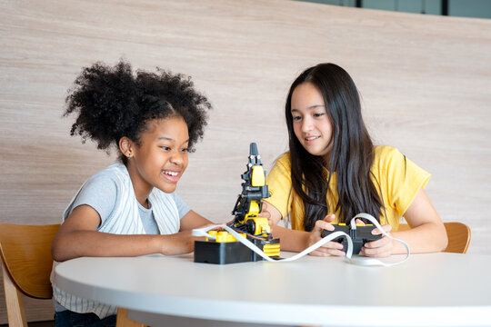 Diverse Girls Learning Programming Through Remote Controller Game, Hands-on STEM Education, Two Young Students Controlling a Prototype with Joy, Friends Operating a Small Robotic Arm