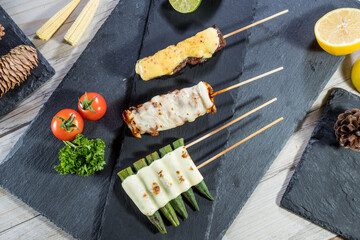 Skewers of grilled meat, chicken, and okra topped with melted cheese, served with tomato, lime, and parsley.
