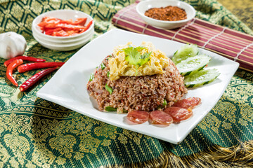 Thai-style fried rice with scrambled egg, Chinese sausage, cucumber, and chili flakes, served on white plate.