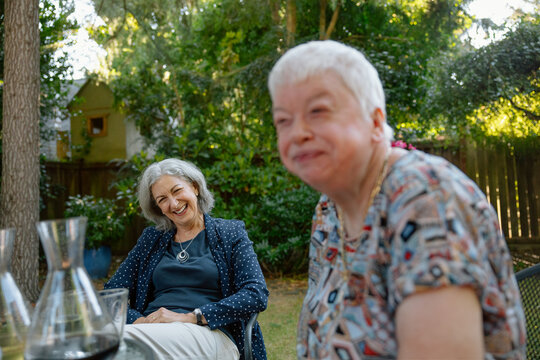Two senior friends share a laugh in a sunny garden gathering