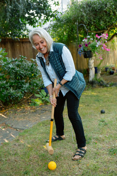 Senior woman playing croquet in garden, smiling as she hits