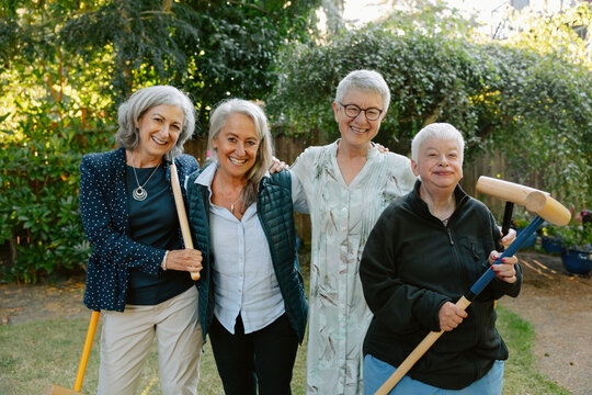 Group of five seniors smiling in a backyard garden with tools