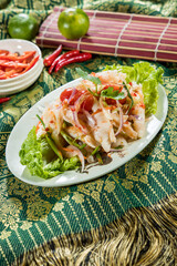 Thai-style spicy salad with onion, tomato, green bean, lettuce, cilantro, and chili flakes on patterned fabric.