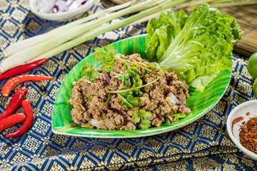 Thai larb salad with minced meat, red onion, green onion, cilantro, and lime juice, served on a leaf plate with traditional Thai ingredients.