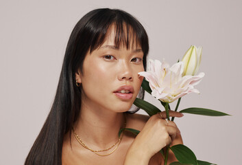 Woman Holding a Flower Poses Softly Against a Neutral Background