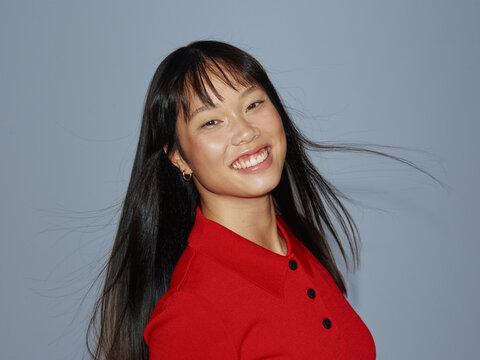 Smiling Woman in Red Shirt With Windblown Hair Against Blue Background