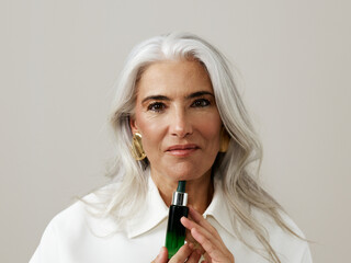 Woman Holding Skincare Bottle With a Soft Smile and Gray Hair