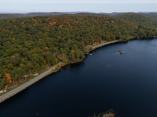 Lakeside road curving through autumn forest hills
