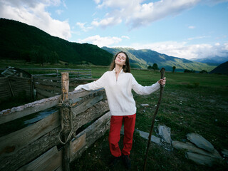 Fototapeta premium Countryside outdoors scene with a woman leaning on a weathered fence, expansive landscape, rolling mountains and a calm valley, conveying freedom and nature connection