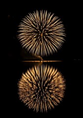Obraz premium Golden Fireworks Burst Reflected in Dark Water Celebration and Night Sky Display Magnificent Pyrotechnics Exploding in Brilliant Light with Mirrored Image