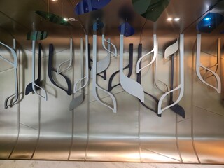 Abstract leaf forms on a curved metal wall, blending organic shapes with a sleek, reflective modern design to create a stylish and contemporary visual aesthetic.
