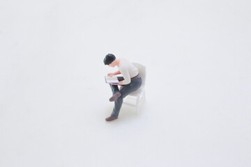 Miniature Man Reading a Book While Seated on a White Chair