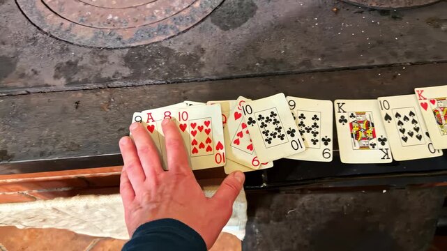 Hand collecting playing cards on stove top showing a combination of face and number cards