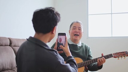 Grandson recording grandpa playing guitar with smiling on comfortable couch