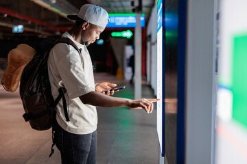 Traveler uses phone and touch screen at transit station.