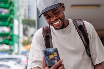 Man with backpack smiles at phone in city setting.