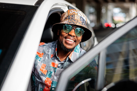 Smiling man in car with hat and sunglasses.