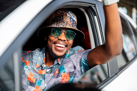 Smiling man in car with hat and sunglasses.