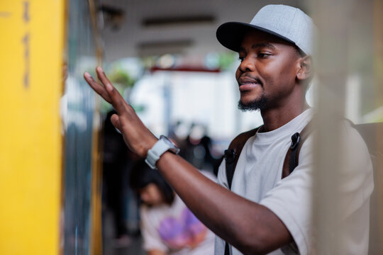 Man in cap touches glass, looking thoughtfully ahead.