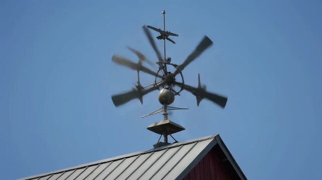A unique metal wind spinner or weather vane on a barn roof against a clear blue sky.