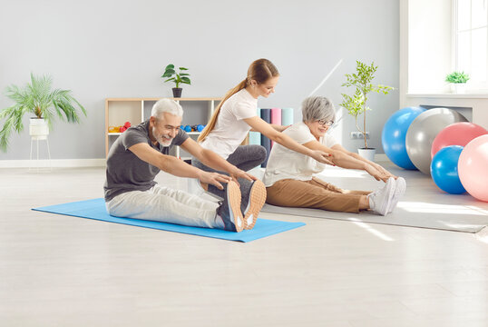Healthy senior couple exercises together with a coach during a rehabilitation session in a fitness gym. Stretching, and practicing to improve health and flexibility during physiotherapy.