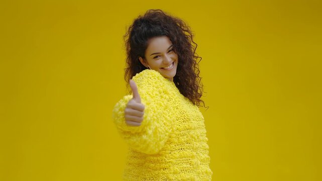 Smiling woman in yellow sweater knit portrait giving thumbs gesture with joyful smile conveying positive confident cheerful mood