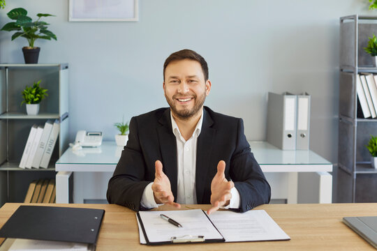 Businessman in office during video call sitting at desk. Employee smiles and gestures as skilled presenter, sharing webinar tips and remote communication online during conference. Technology concept