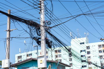 A heavily burdened and cluttered utility pole in a suburban setting, supporting a dangerously dense network of black electrical and telecommunication wires and cables.