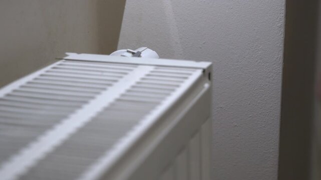 Hand adjusting heater thermostat to increase temperature, showing winter heating control, home comfort, warmth regulation and energy management.
