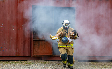 Firefighter in fireproof clothe is carrying young kid out of the burning building full of ash and...