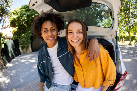 Portrait of couple sitting on car trunk smiling at camera. Fisheye.