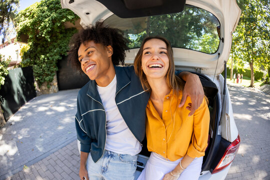 Portrait of young couple sitting on car trunk smiling. Fisheye.