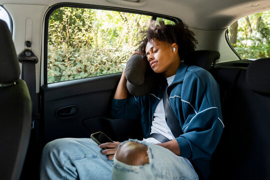 man traveling in car sleeping with travel pillow using earbuds