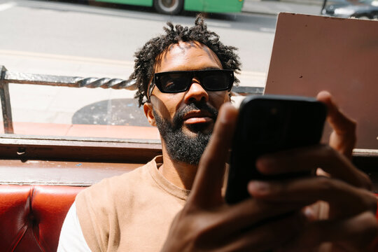 Black Man Scrolling on His Phone at an Irish Pub During the Day