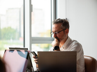 Thoughtful Businessman Using Phone by the Window in Front of Computer