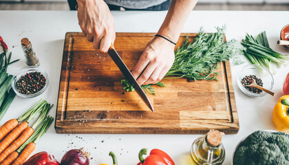 Overhead view of a person chopping fresh green herbs on a wooden cutting board.