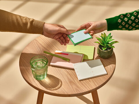 Two hands exchanging a small card over a tidy wooden table