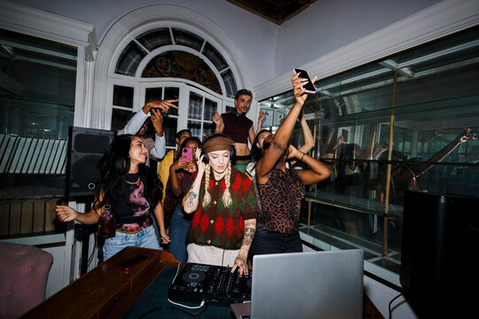 Female dj playing music for young friends dancing exciting party - Powered by Adobe