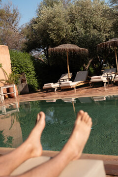 A man sits by a pool on a sunbed
