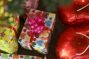 Joyful gift box present with heart pattern for love celebration. package has pink bow, red ribbon, and red heart balloons in background for special party
