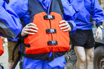 Person holding an orange life vest as safety equipment before an outdoor activity. Group wearing blue jacket feel prepared and focused for water adventure ahead