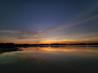 Fototapeta premium Winter sunset over a calm reservoir with golden reflections and soft clouds. Peaceful evening sky glowing with warm light across the still water.