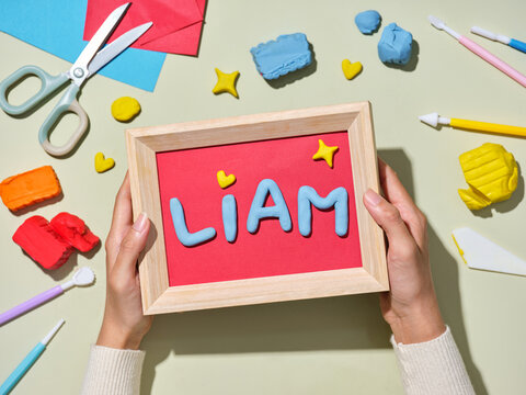 A person holding a framed artwork with the name Liam made of clay.