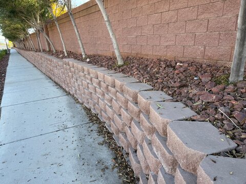 Desert Red Stone Retaining Wall: Landscaped retaining wall built with red bricks and natural red rocks in a suburb.