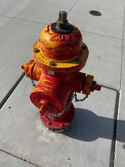Red and Yellow Fire Hydrant: Close up of a red municipal fire hydrant painted with yellow brush strokes.