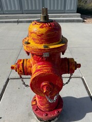 Red and Yellow Fire Hydrant: Close up of a red municipal fire hydrant painted with yellow brush strokes.