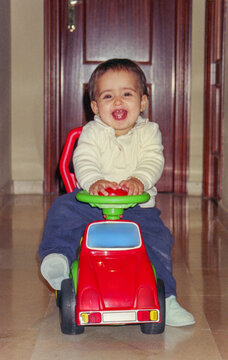 Fun portrait of baby happily riding toy car at home