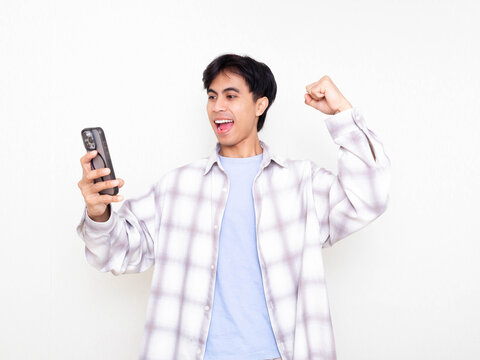 Young man celebrating while checking his smartphone, showing excitement about digital business results on a clean white background.